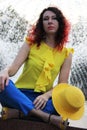 portrait of a brunette sitting in the Lotus position at the fountain. A woman sit in the lotus pose with a yellow hat on her lap