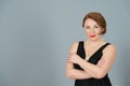 Portrait of American Brunette woman on grey background. Lady in black dress with perls and crossed hand on chest.