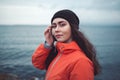 Portrait of a brunette woman with a mysterious look with long hair, wearing a hat and an orange jacket. In the background the sea Royalty Free Stock Photo