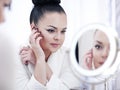 Portrait of a brunette woman putting on make up in front of the mirror