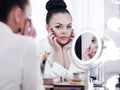 Portrait of a brunette woman putting on make up in front of the mirror