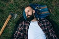 Portrait brutal bearded and moustached woodcutter hipster Gypsy man in the forest with ax. Man lying on the grass and dreams