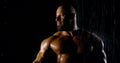 Portrait of a brutal muscular bald bearded male bodybuilder close-up on a black background, he poses, shows biceps, he