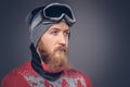 Portrait of a brutal redhead bearded male in a winter hat with protective glasses dressed in a red sweater, posing with