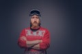 Portrait of a brutal redhead bearded male in a winter hat with protective glasses dressed in a red sweater, posing with