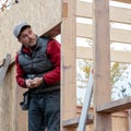 Portrait of builder with an electric screwdriver in his hands. Male worker builds wooden structure with screwdriver.