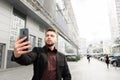 Portrait of a business man with a beard and dressed in a suit, walking around the streets of the city and takes selfie Royalty Free Stock Photo