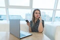 Portrait of a business woman with a phone in her hands sitting on a white laptop in a restaurant with a stylish design. Royalty Free Stock Photo