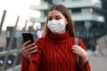 Portrait of business woman with protective mask walking in modern city background using smartphone Royalty Free Stock Photo