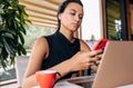 Portrait of business woman working on laptop indoor in a cafe. Image of serious young female texting messages on mobile phone with