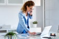 Business young woman talking on the mobile phone while using her laptop in the office. Royalty Free Stock Photo