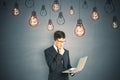 Portrait of a businessman with a laptop in his hands standing in front of a gray wall with glowing lightbulbs. Idea concept