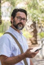 Portrait of businessman using cellphone outdoor at the park with roaming internet connection - adult bearded man with glasses