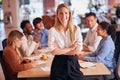 Portrait Of Businesswoman With Colleagues In Background Sitting Around Table In Open Plan Office