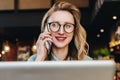 Portrait businesswoman in glasses sitting in cafe in front of laptop,talking on phone.Girl blogger communicates by phone Royalty Free Stock Photo