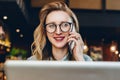 Portrait businesswoman in glasses sitting in cafe in front of laptop,talking on phone.Girl blogger communicates by phone Royalty Free Stock Photo