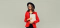 Portrait of businesswoman with laptop wearing red blazer jacket, eyeglasses, round hat on gray background, happy elegant woman Royalty Free Stock Photo