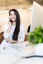 Portrait of a businesswoman sitting on her workplace in the office talking on the phone, looking at pc screen Royalty Free Stock Photo