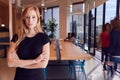 Portrait Of Businesswoman Standing In Busy Modern Open Plan Office With Colleagues In Background