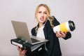 Portrait busy angry young businesswoman in formal suit with laptop, folder, box, coffee to go in hands talking on phone
