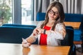 Portrait of busy beautiful stylish brunette young woman in glasses sitting and checking time on her smart watch with serious face Royalty Free Stock Photo
