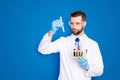 Portrait of busy concentrated scientist with stubble in white lab coat, gloves analysing, looking at test tubes with Royalty Free Stock Photo