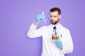 Portrait of busy concentrated scientist with stubble in white lab coat, gloves analysing, looking at test tubes with Royalty Free Stock Photo