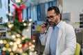 Portrait of busy doctor phone calling in emergency room, decorated for Christmas. Mature male doctor working a Royalty Free Stock Photo