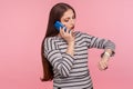 Portrait of busy, impatient, dissatisfied woman in striped sweatshirt talking on mobile phone checking time