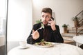 Portrait of a busy man who talks on the phone and eats a salad with a fork in a cozy restaurant, looking away Royalty Free Stock Photo