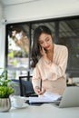 Busy millennial Asian businesswoman is on the phone with a business client, standing at her desk