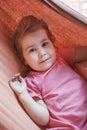 Portrait of calm Caucasian little girl laying in fabric hammock and looking at camera