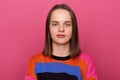 Portrait of calm cute attentive young adult Caucasian woman with brown hair wearing colorful jumper posing isolated over pink