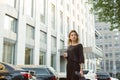 Portrait of calm elegant woman looking aside dressed in grey blouse and plack pants holding coffee in front of skyscraper. Young Royalty Free Stock Photo