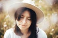 Portrait of calm hipster girl in hat relaxing in wildflower meadow, traveling in sunny mountains. Stylish carefree woman enjoying