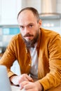 Portrait calm man working at laptop at kitchen home interior. Bald bearded 30s man looking at the camera Royalty Free Stock Photo