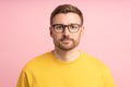 Portrait calm pensive bearded middle aged man in glasses looking at camera on pink background.