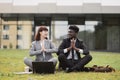 Multiracial coworkers, sitting on green grass outside, and doing yoga meditation in namaste pose Royalty Free Stock Photo