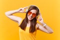 Portrait of calm smiling young woman in orange glasses listening music in headphones copy space isolated on yellow Royalty Free Stock Photo