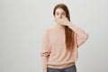 Portrait of calm tired ginger girl covering mouth with hand, standing over gray background in casual outfit. Body