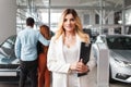 Portrait of a car sales manager woman. Auto dealership representative against the background of a couple who chooses a car