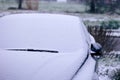 A portrait of a car starting to get snowed under during a blizzard. The snow already covers the windshield of the car making it