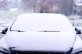 A portrait of a car starting to get snowed under during a snowstorm. The snow already covers the windshield of the vehicle making