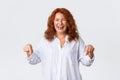 Portrait of carefree cheerful redhead woman laughing and pointing fingers down happy. Amused beautiful lady, female