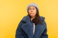 Portrait of carefree girl wearing warm winter hat and fur coat, stylish urban outfit, standing with closed eyes showing tongue Royalty Free Stock Photo