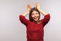 Portrait of carefree happy brunette girl making funny bunny ears with hands on head, childish behavior