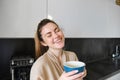 Portrait of carefree smiling woman drinking coffee, standing in kitchen with delighted, pleased face expression, waking