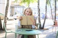 Portrait of carefree, smiling young woman with notebook and pen, sitting in outdoor cafe near table, writing in journal Royalty Free Stock Photo