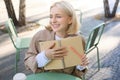 Portrait of carefree, smiling young woman with notebook and pen, sitting in outdoor cafe near table, writing in journal Royalty Free Stock Photo