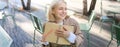 Portrait of carefree, smiling young woman with notebook and pen, sitting in outdoor cafe near table, writing in journal Royalty Free Stock Photo